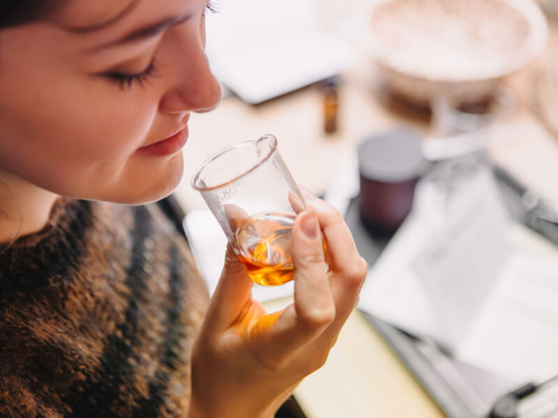 Woman smelling a beaker of orange-coloured essential oil